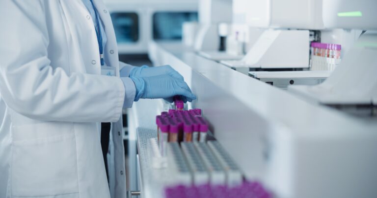 Laboratorijos darbuotojas tvarko mėginius violetiniais dangteliais